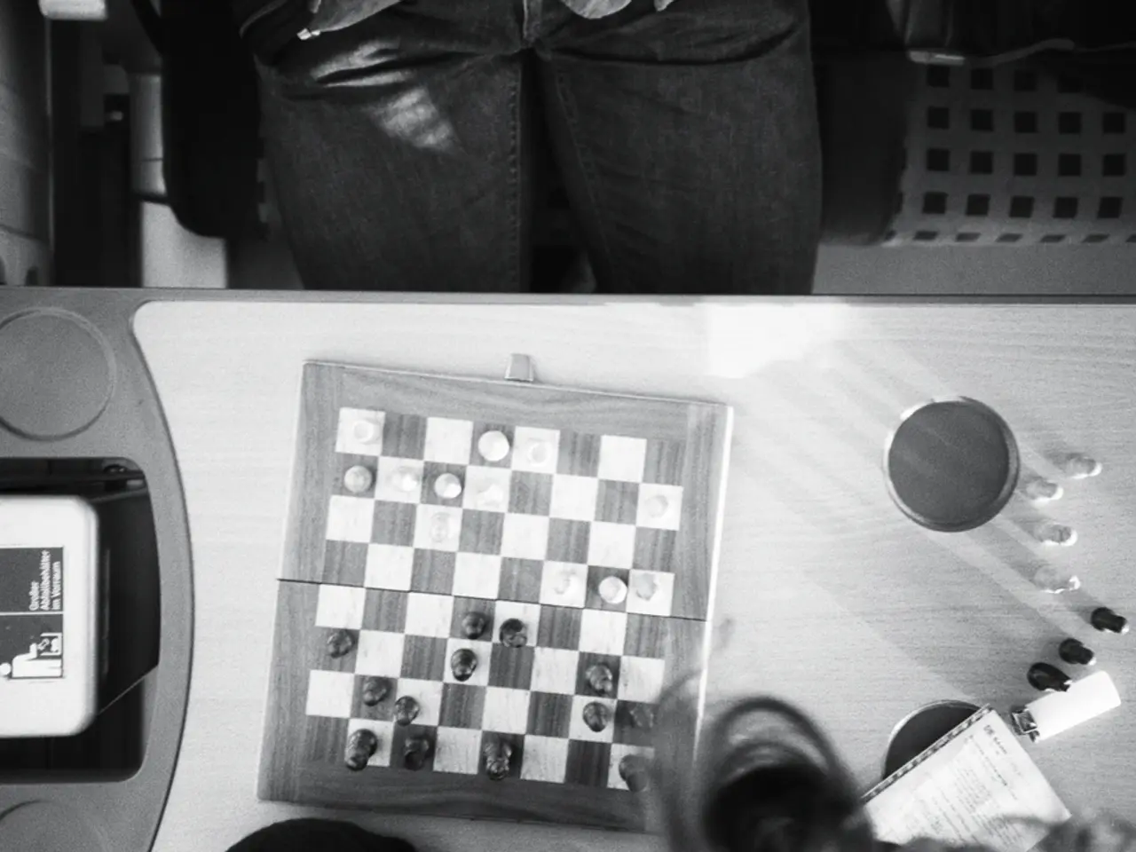 In this image I can see a chess board and few objects on the table. I can see a person sitting on...