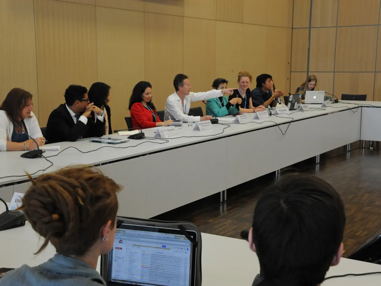 This picture is clicked inside a conference hall. We see many people sitting on a chair. There are...