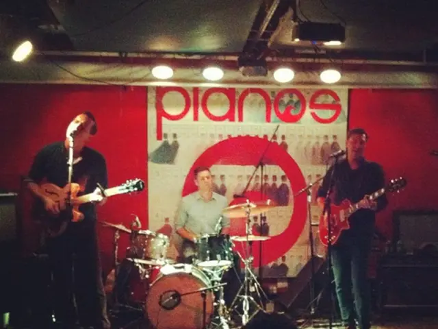 This image is clicked in a concert. There are three men on the dais. In the middle, the man sitting...