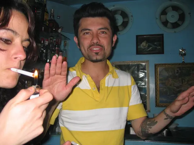 In the image we can see there is a person standing and a woman is lighting cigarette. Behind there...