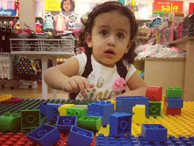 In the picture there is a baby playing with blocks of a color blocks game, behind the baby there...