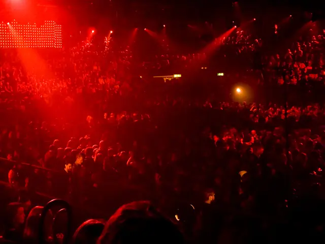 In this image I can see in the middle there are lot of people, at the top there are focus lights.