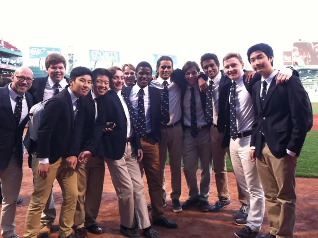 In this image there are few men standing and smiling. They are wearing suits. Behind them there's...