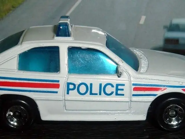 In this picture there is a white color police car toy. Behind there is a road poster.